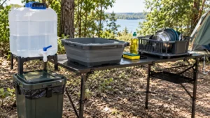 Estação de higienização em camping com reservatório de água potável, bacia, detergente, esponja, escorredor e recipiente para resíduos.